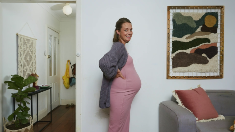 Pregnant woman standing side-on next to a wall in a living room