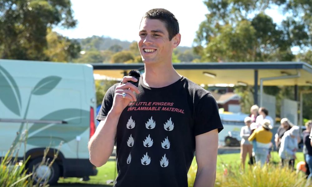 A man with short brain hair smiles and hold a small microphone. 