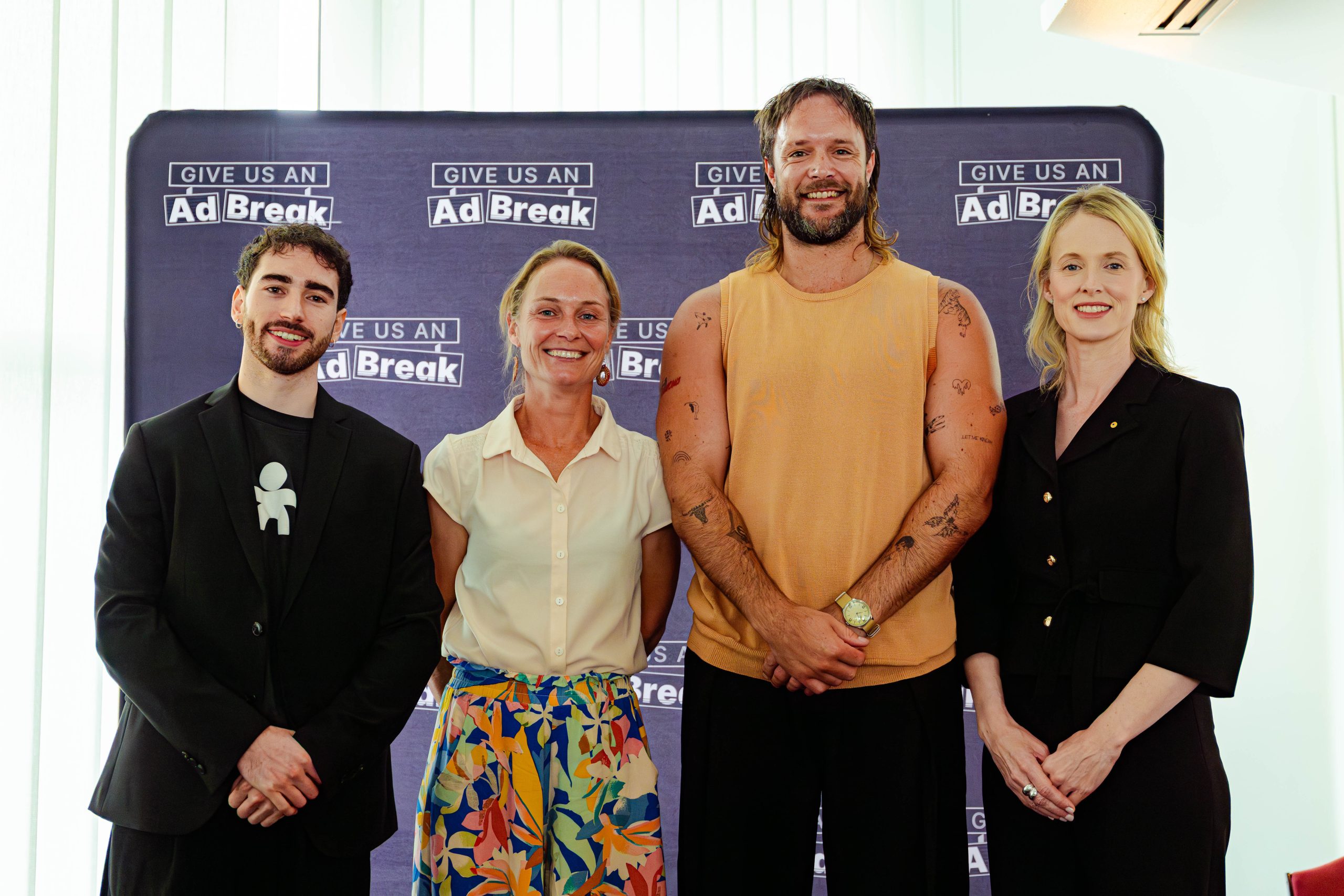 Daniel Datnow-Jamieson, Kathryn Backholer, Mitch Brown and Bronwyn King stand together in front of a banner with the Give Us An Ad Break logo printed on it.