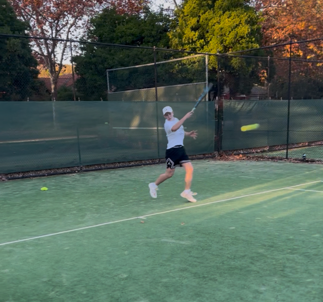 A young boy plays tennis on an outside court.