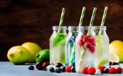 Four drinks with straws, lined up in a row and surrounded by lemons and limes