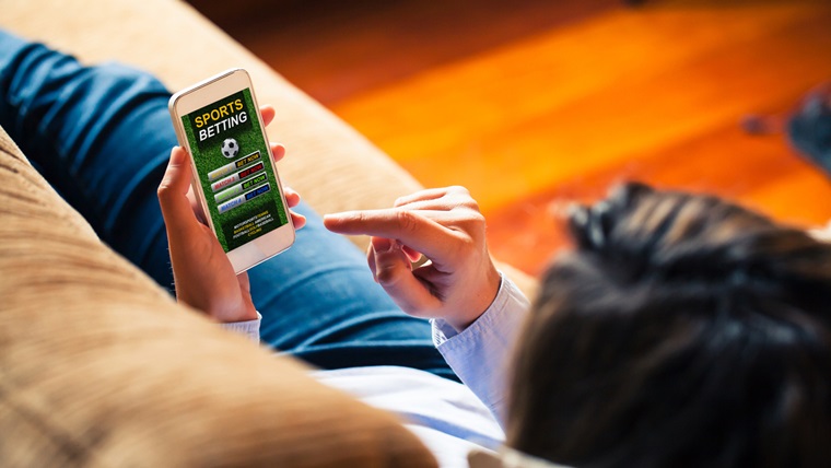 Person laying on couch looking at a phone with a gambling sports app on the screen