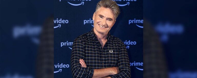 Dave Hughes (Australian TV personality) standing in front of a banner