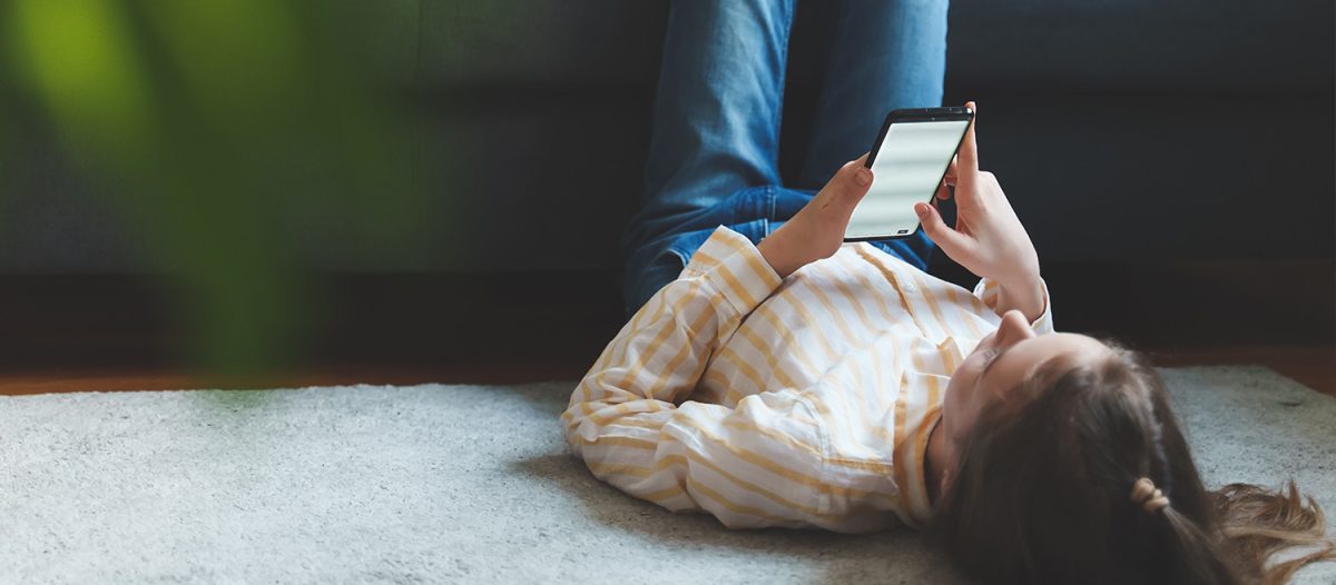 A young girl lying on her back on the floor while using a mobile phone.