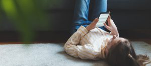 A young girl lying on her back on the floor while using a mobile phone.
