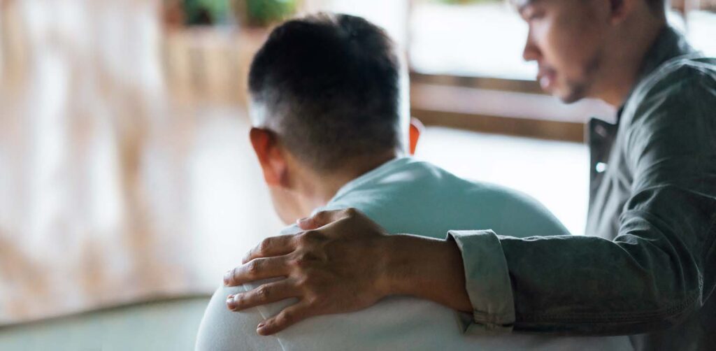 Rear view of son and elderly father sitting together at home