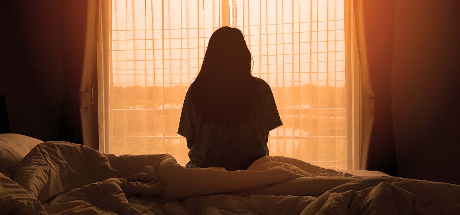 Young woman sitting on bed, looking away from camera and out of window