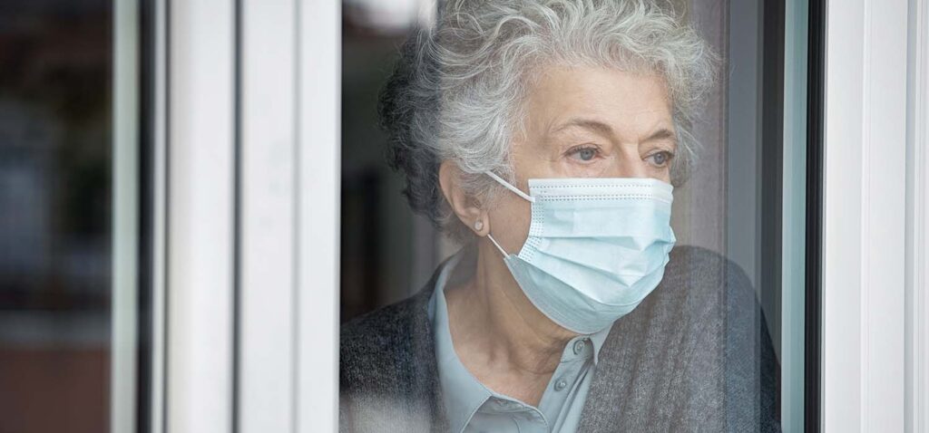 Elderly lady wearing mask and looking out of window