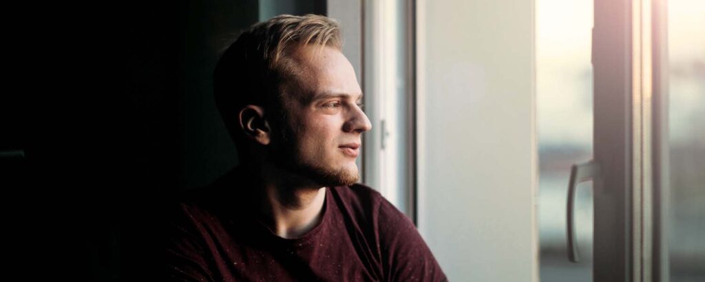 Young man looking solemnly out of a window